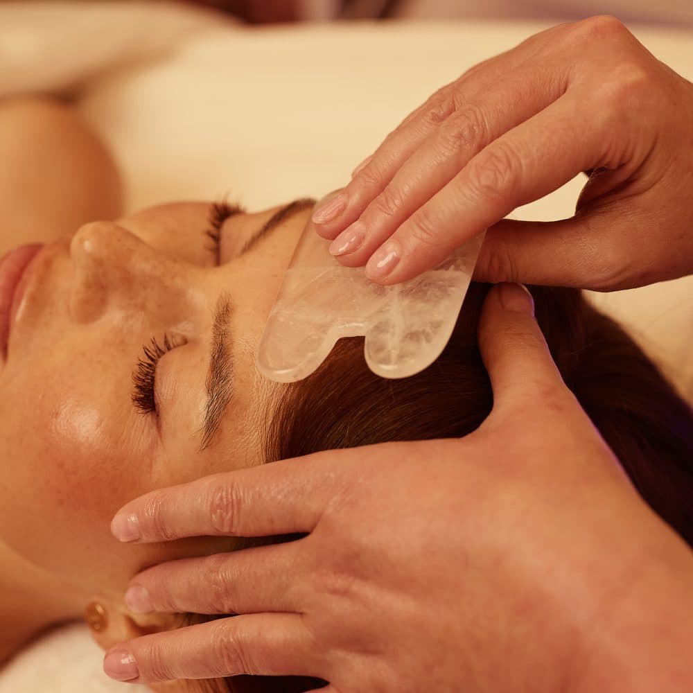 Zhanna Graeff drawing a gua sha stone across the forehead
